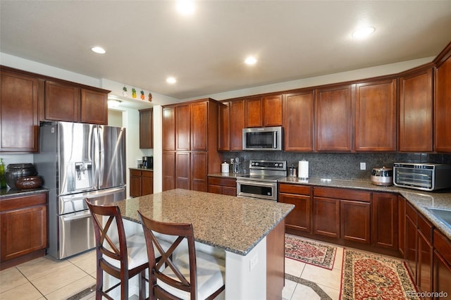 kitchen featuring light tile patterned floors, stone counters, a toaster, stainless steel appliances, and decorative backsplash