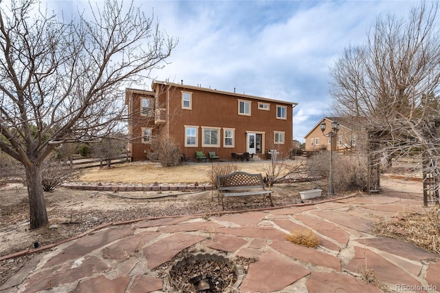 rear view of house featuring a patio area, a fire pit, and stucco siding