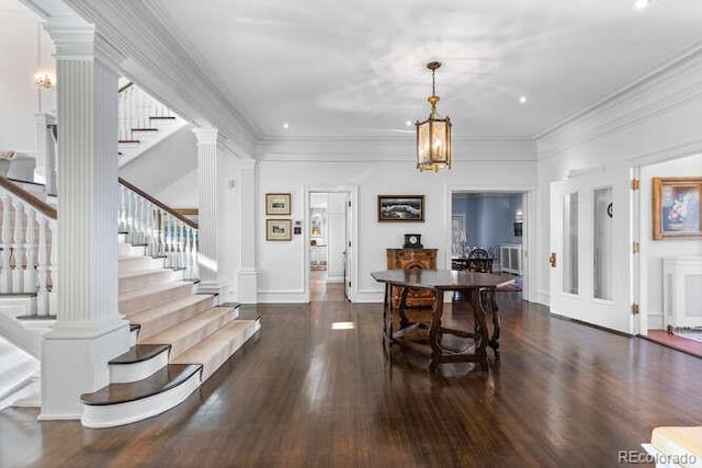 dining space with dark wood-type flooring, ornamental molding, decorative columns, and a chandelier