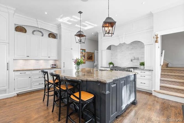 kitchen featuring pendant lighting, a center island with sink, light stone counters, white cabinets, and a kitchen bar