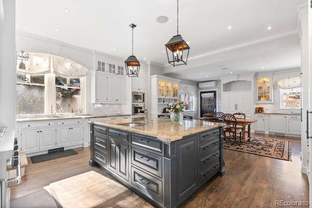 kitchen featuring sink, white cabinetry, a center island, stainless steel microwave, and light stone countertops