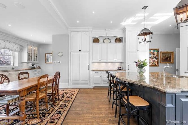 kitchen with white cabinetry, an island with sink, sink, hanging light fixtures, and light stone counters