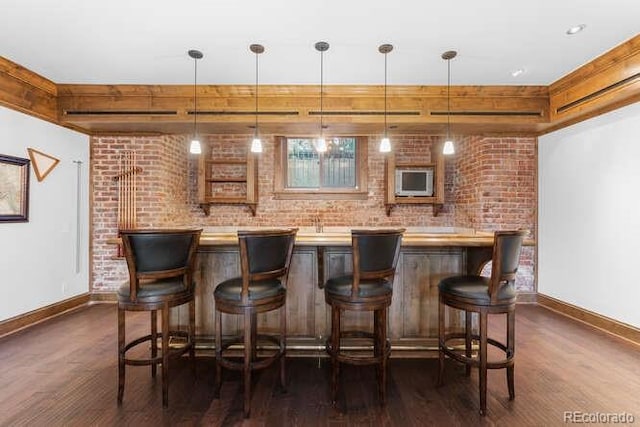 bar with dark wood-type flooring, brick wall, and hanging light fixtures