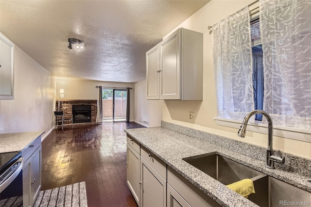 2223 S Buckley Rd Unit 102, Aurora, CO 80013 - kitchen featuring stainless steel electric stove, a textured ceiling, open floor plan, a brick fireplace, and light stone counters