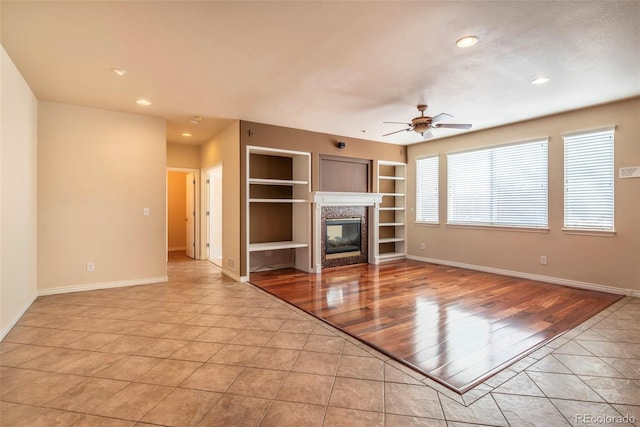 unfurnished living room with a high end fireplace, built in features, ceiling fan, and light tile patterned flooring