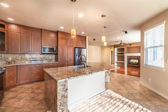 kitchen with sink, backsplash, an island with sink, decorative light fixtures, and appliances with stainless steel finishes