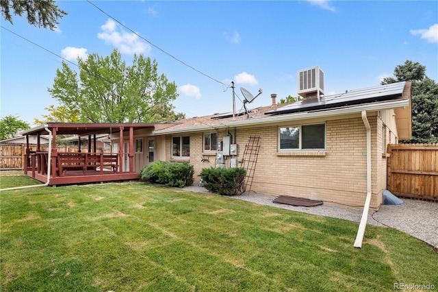 back of house with a wooden deck, a lawn, and solar panels