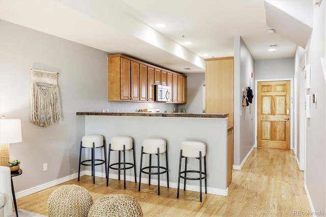 3030 Wyandot St Unit 4, Denver, CO 80211 - kitchen featuring stainless steel microwave, a breakfast bar, light wood finished floors, brown cabinets, and recessed lighting