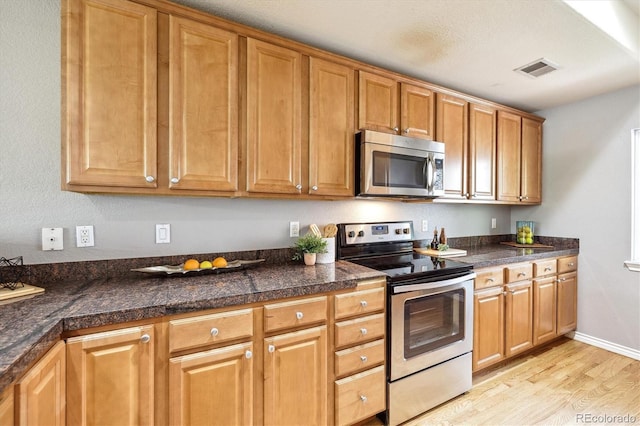 3030 Wyandot St Unit 4, Denver, CO 80211 - kitchen featuring stainless steel appliances, light wood finished floors, tile counters, brown cabinetry, and baseboards