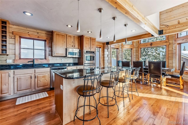 kitchen featuring a breakfast bar, light wood-style floors, beamed ceiling, stainless steel appliances, and a sink