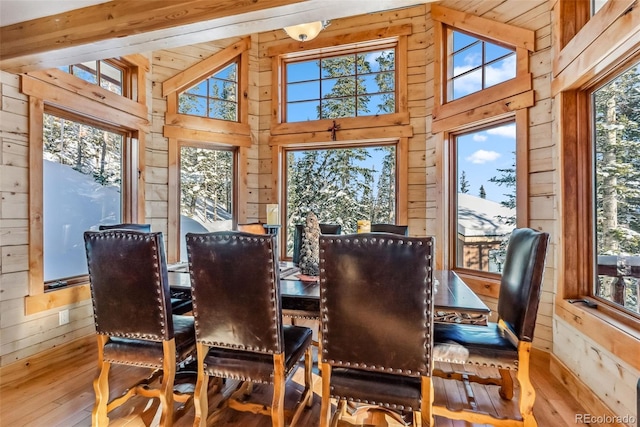 dining room with high vaulted ceiling, wood walls, and hardwood / wood-style flooring