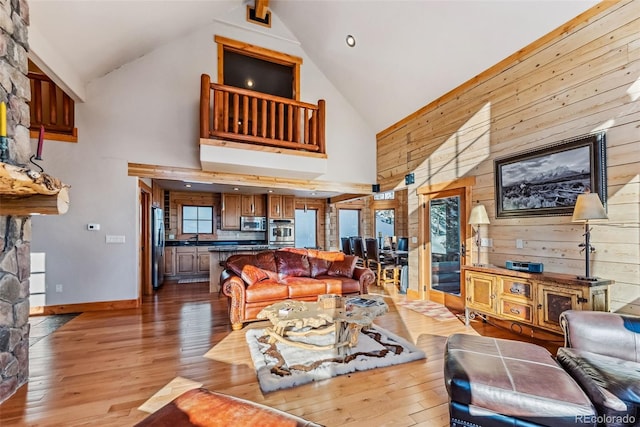 living area featuring high vaulted ceiling, wooden walls, light wood-style floors, and baseboards