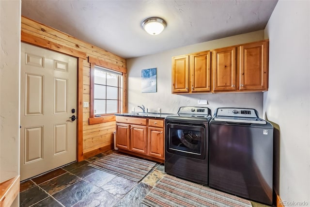 washroom featuring independent washer and dryer, stone finish floor, wood walls, a sink, and cabinet space