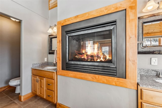 bathroom with baseboards, a multi sided fireplace, toilet, vanity, and tile patterned floors