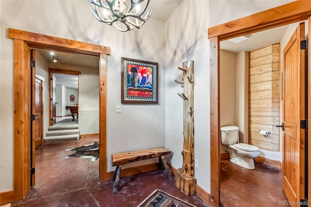 hall featuring visible vents, baseboards, a notable chandelier, and finished concrete flooring