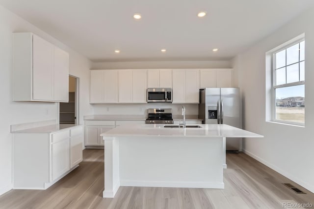 kitchen featuring white cabinetry, sink, stainless steel appliances, a center island with sink, and light wood-type flooring