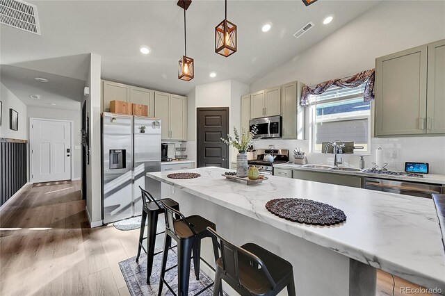 kitchen with hanging light fixtures, stainless steel appliances, light hardwood / wood-style floors, and light stone countertops