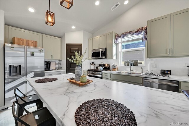 kitchen with sink, appliances with stainless steel finishes, hanging light fixtures, backsplash, and light stone counters