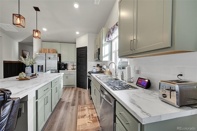 kitchen with sink, tasteful backsplash, hanging light fixtures, light wood-type flooring, and stainless steel appliances