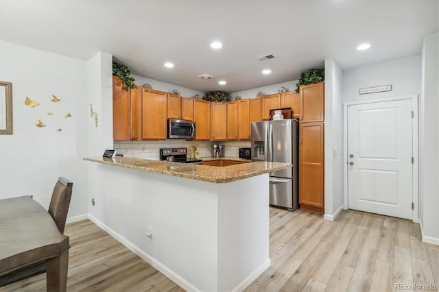 kitchen with tasteful backsplash, light hardwood / wood-style flooring, kitchen peninsula, stainless steel appliances, and light stone countertops