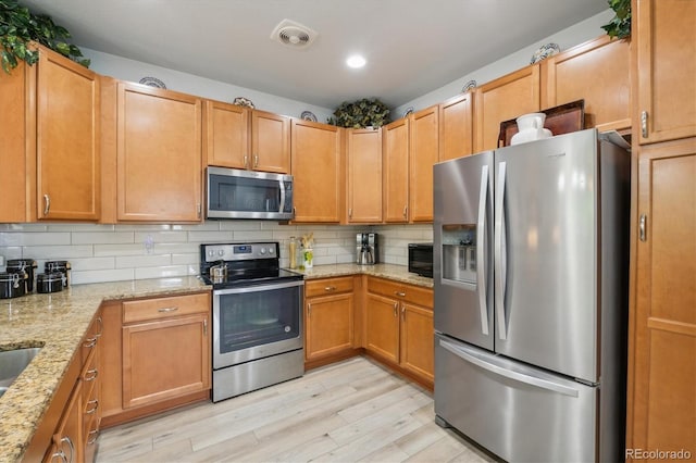 kitchen with stainless steel appliances, light stone countertops, light hardwood / wood-style flooring, and backsplash