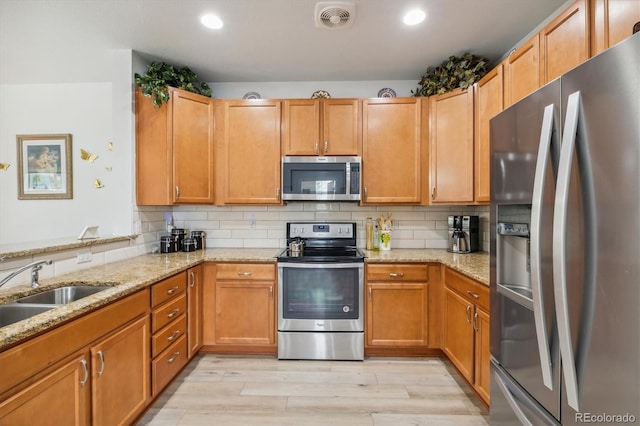 kitchen with sink, backsplash, stainless steel appliances, light stone countertops, and light wood-type flooring