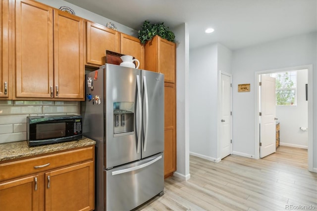 kitchen featuring stainless steel refrigerator with ice dispenser, light stone countertops, light hardwood / wood-style floors, and backsplash