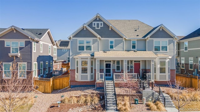 view of front of house featuring covered porch, a shingled roof, brick siding, fence, and stairs