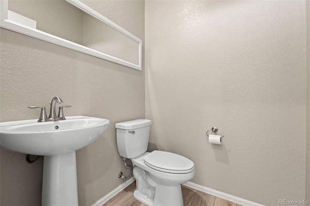 bathroom with baseboards, a sink, toilet, and wood finished floors