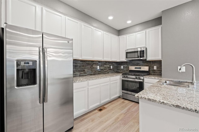 kitchen featuring visible vents, light wood-style flooring, a sink, stainless steel appliances, and backsplash