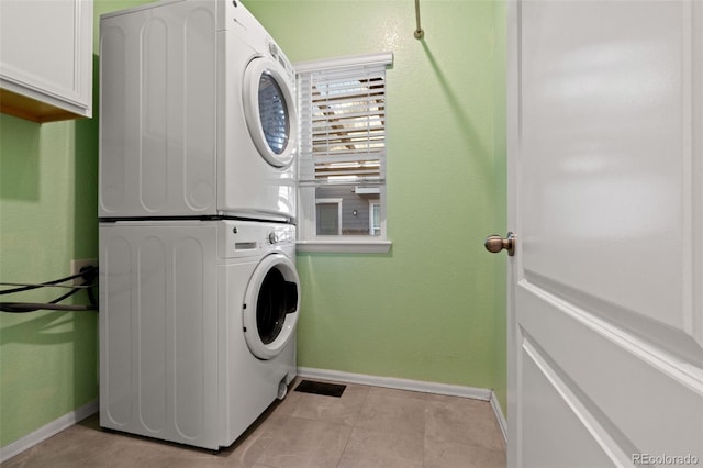 clothes washing area featuring cabinet space, light tile patterned floors, baseboards, and stacked washer / drying machine