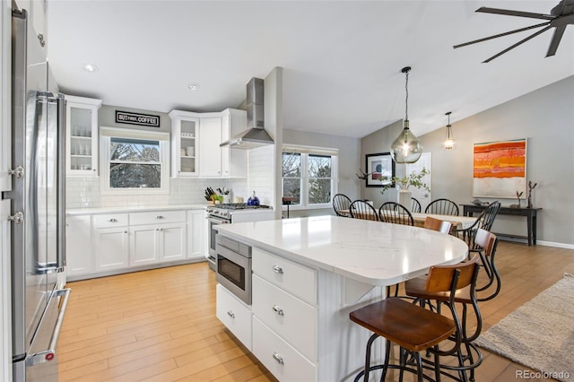 kitchen featuring a kitchen bar, glass insert cabinets, white cabinets, a kitchen island, and wall chimney exhaust hood