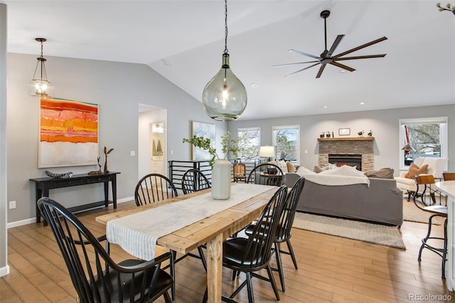 dining room featuring lofted ceiling, light wood finished floors, a fireplace, and a healthy amount of sunlight