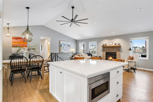 kitchen with white cabinets, stainless steel microwave, open floor plan, a center island, and hanging light fixtures