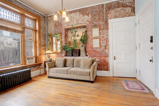 living room featuring radiator, light hardwood / wood-style floors, a chandelier, and brick wall