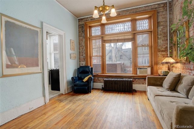 living area featuring brick wall, a notable chandelier, light hardwood / wood-style floors, ornamental molding, and radiator heating unit