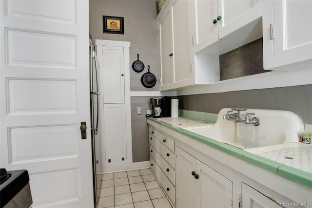 kitchen with sink, light tile patterned floors, tile counters, and white cabinetry