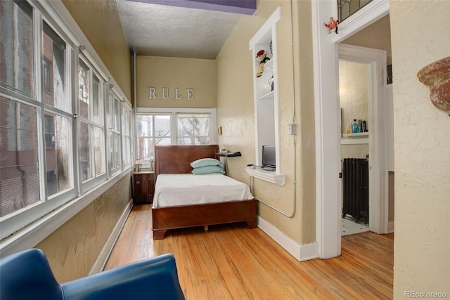 bedroom with light wood-type flooring, radiator, and a textured ceiling