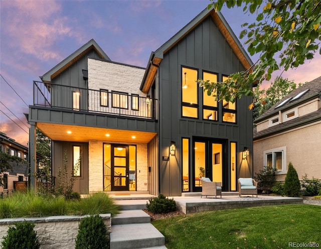 back house at dusk with a balcony, a yard, and a patio