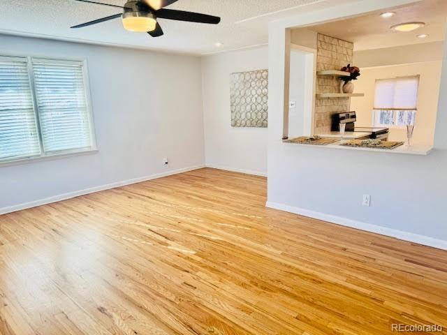 unfurnished living room featuring ceiling fan, light wood-type flooring, a stone fireplace, and a textured ceiling