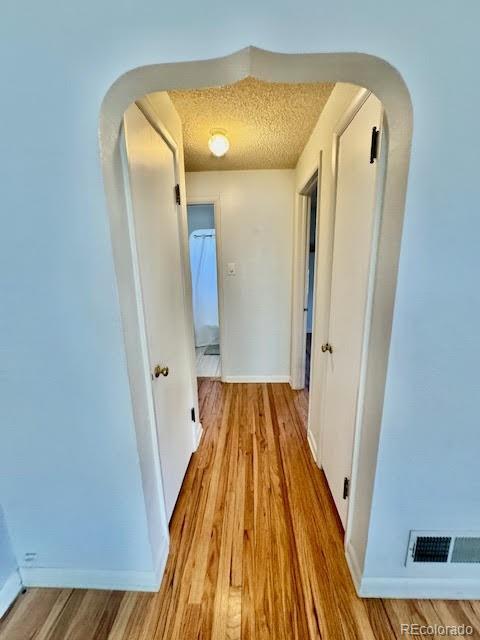 corridor with light wood-type flooring and a textured ceiling