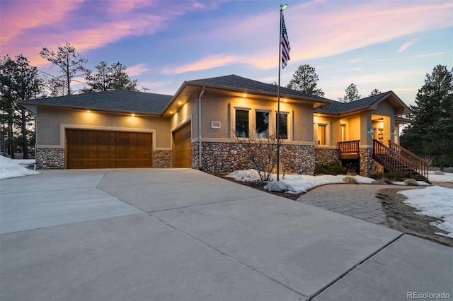 prairie-style home with stone siding, concrete driveway, an attached garage, and stucco siding