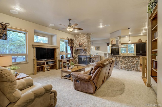 living area with a ceiling fan, light colored carpet, and a stone fireplace