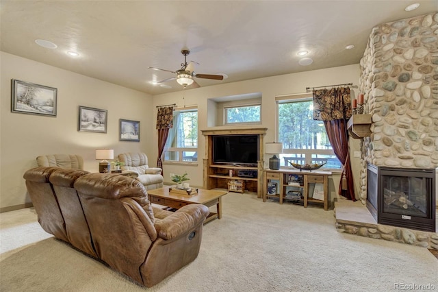 carpeted living room featuring a stone fireplace, a ceiling fan, and baseboards