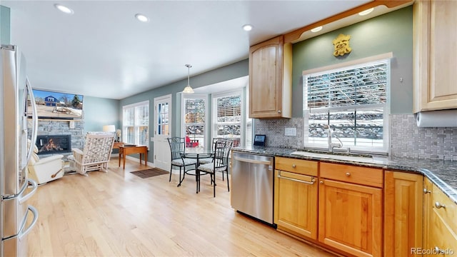 kitchen with a fireplace, a sink, decorative backsplash, stainless steel appliances, and light wood-style floors