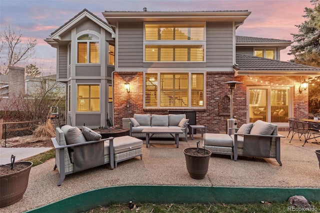 back of property at dusk featuring fence, a patio, an outdoor living space, and brick siding