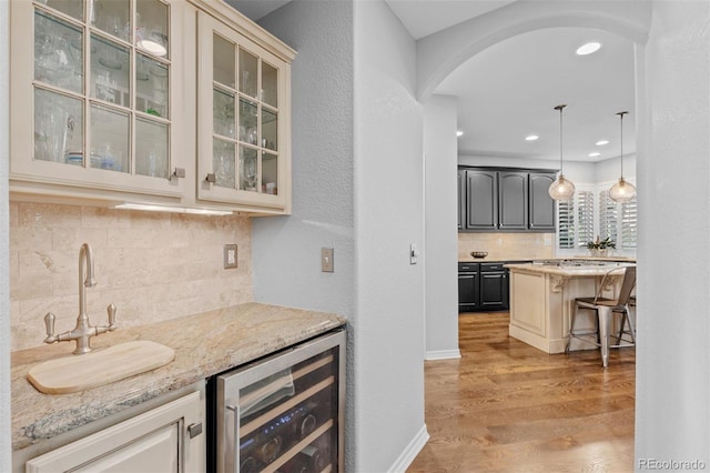 bar with light wood finished floors, beverage cooler, a sink, arched walkways, and backsplash