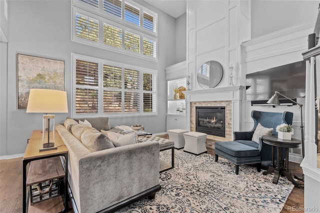living area featuring wood finished floors, baseboards, a high ceiling, and a glass covered fireplace