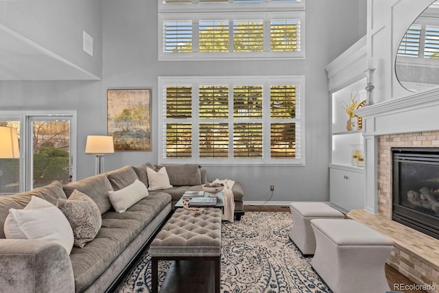 living area with a fireplace, a towering ceiling, baseboards, and wood finished floors