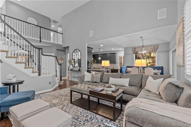 living area featuring stairs, a high ceiling, an inviting chandelier, and dark wood-style floors